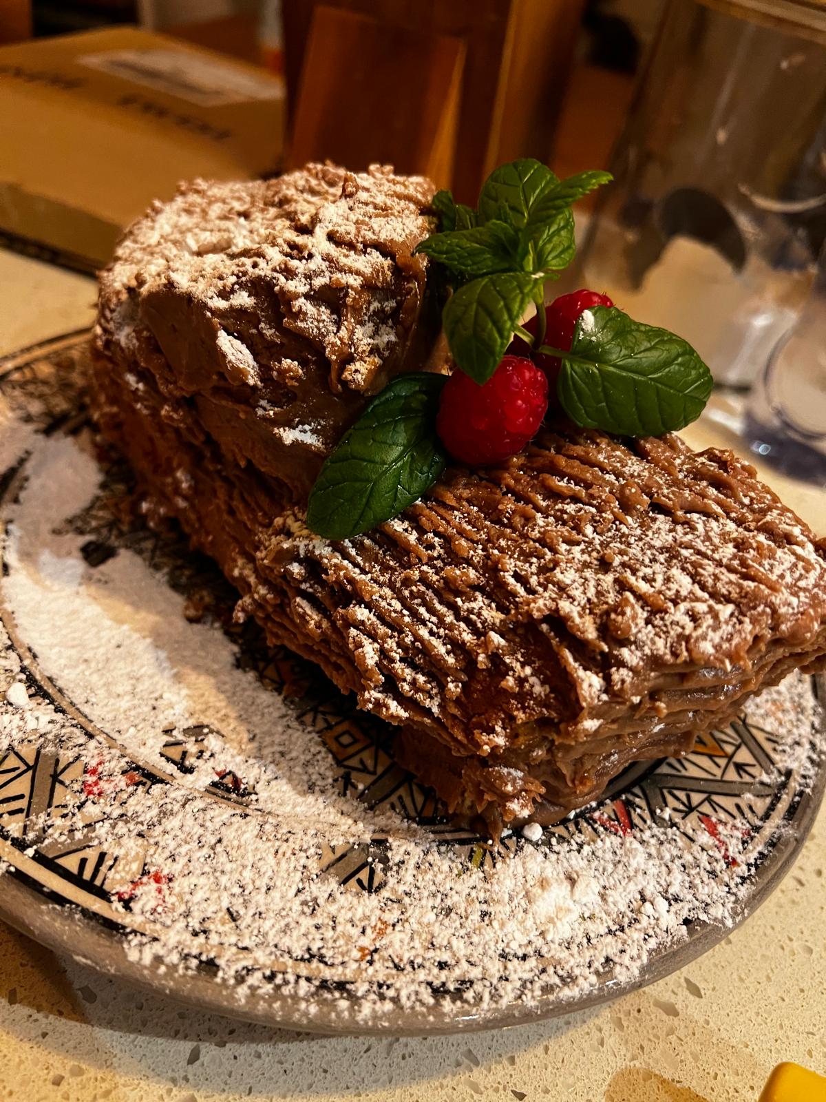 Chocolate Yule log decorated with berries, leaves and icing sugar